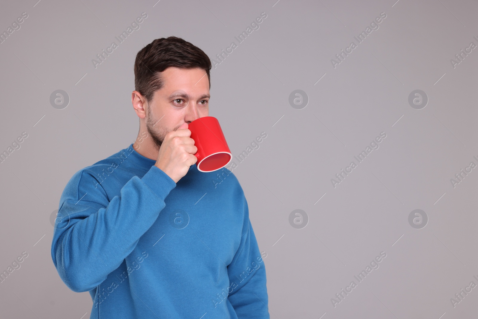 Photo of Man drinking from red mug on grey background. Space for text