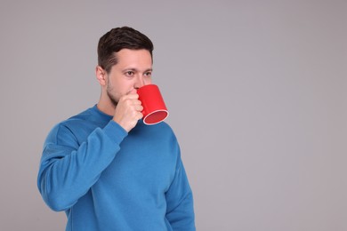 Man drinking from red mug on grey background. Space for text