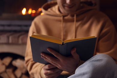 Photo of Man reading book near fireplace at home, closeup