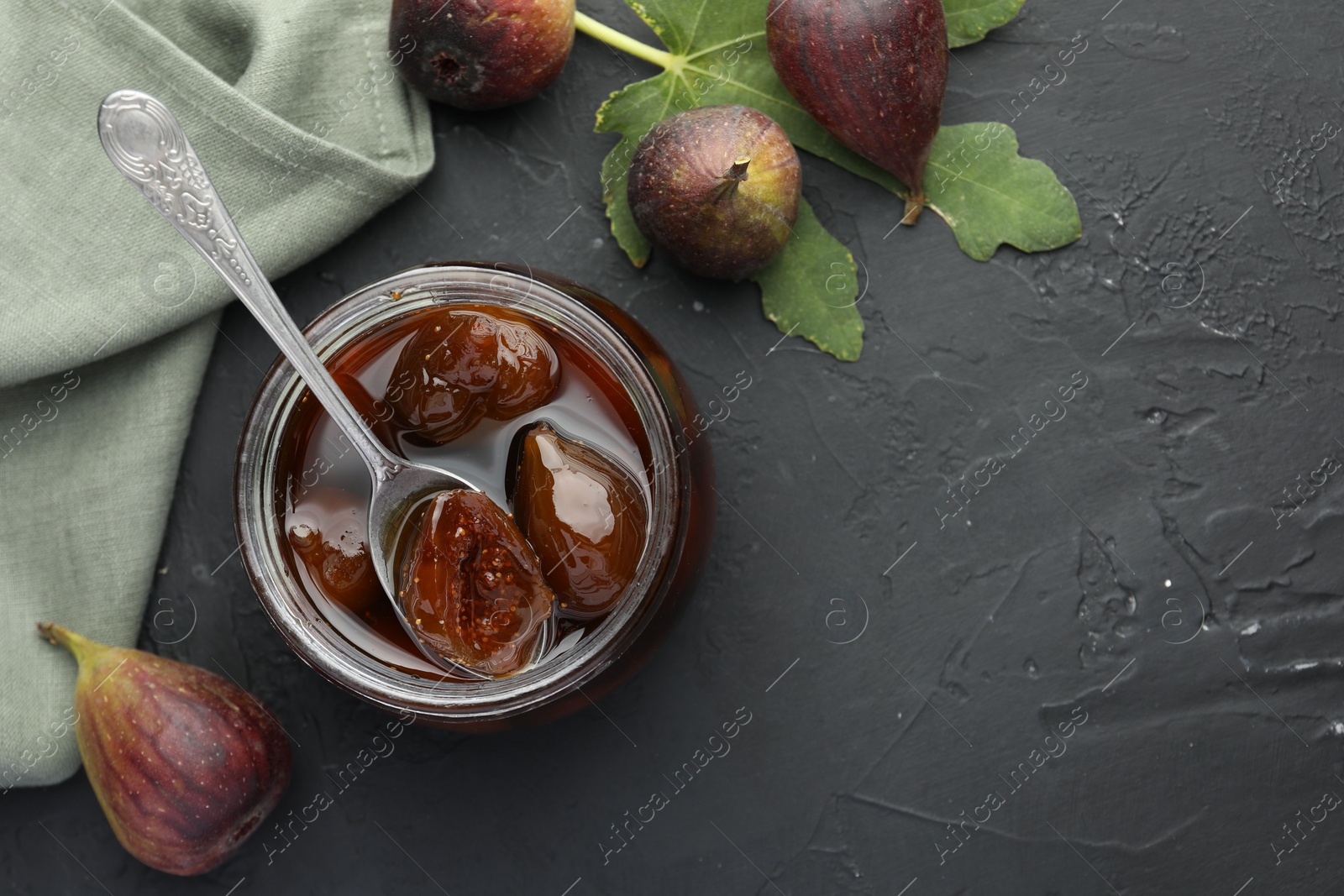 Photo of Jar of tasty sweet jam and fresh figs on black table, flat lay. Space for text