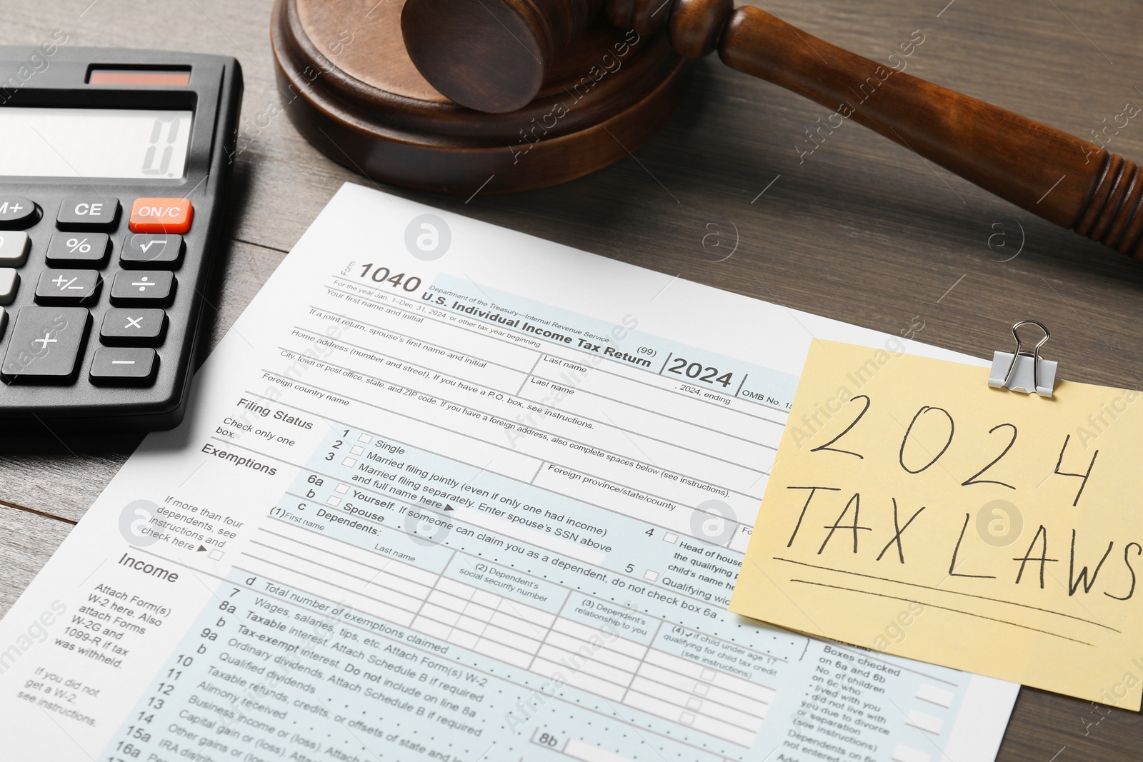 Photo of 2024 tax laws. Form, paper note, calculator and gavel on wooden table, closeup