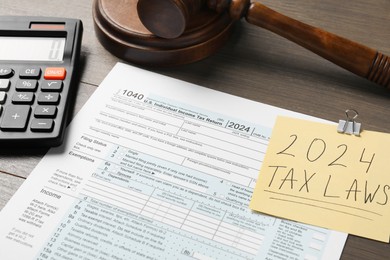 2024 tax laws. Form, paper note, calculator and gavel on wooden table, closeup