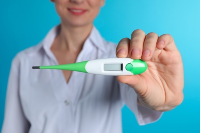 Photo of Female doctor holding digital thermometer on color background, closeup. Medical object