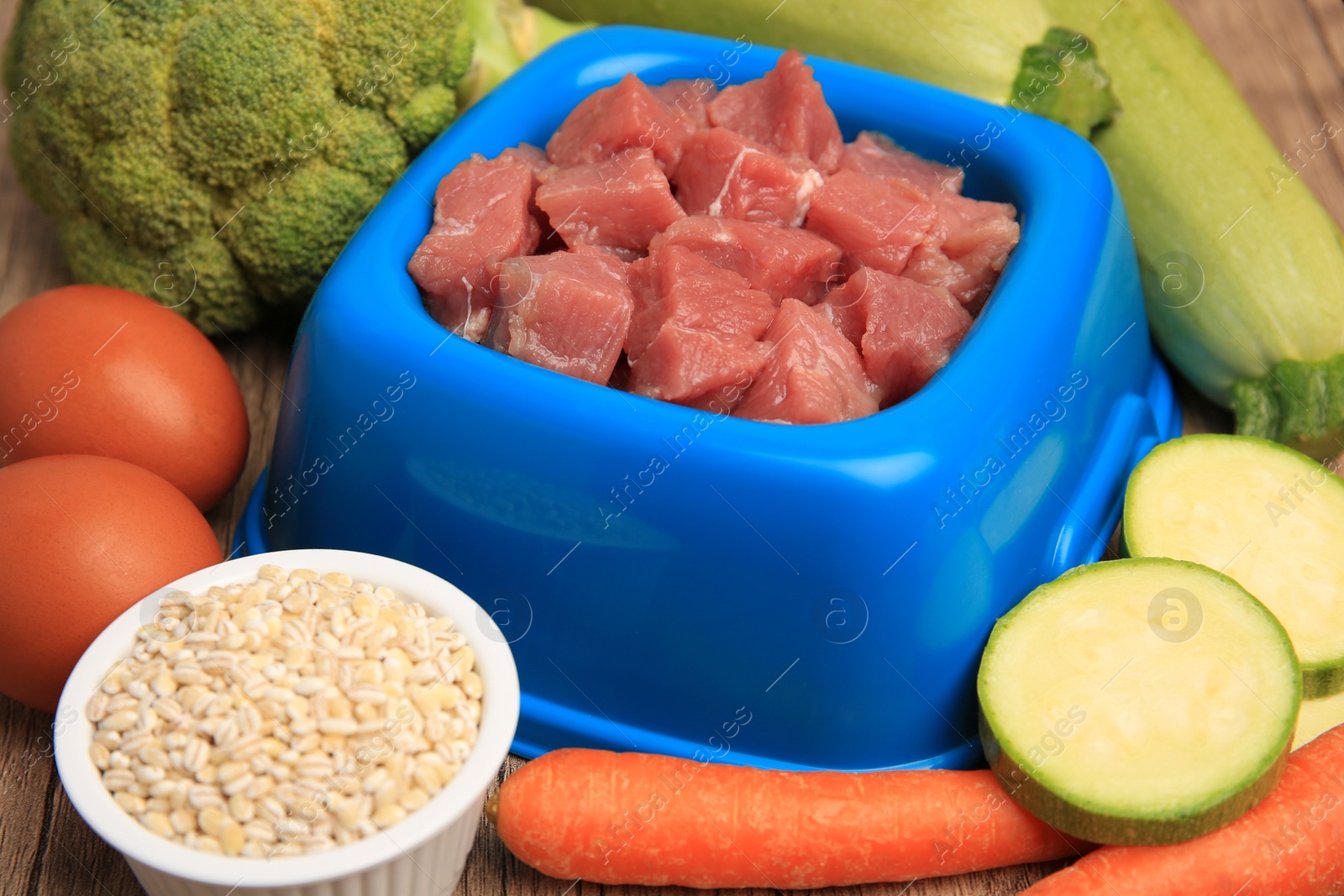 Photo of Raw meat in bowl and healthy products for pet on wooden background, closeup