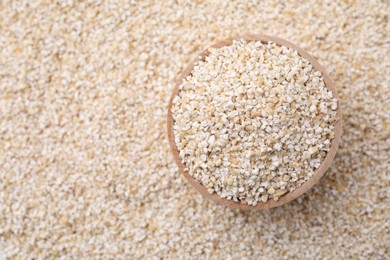 Photo of Wooden bowl on raw barley groats, top view. Space for text