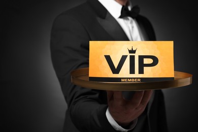Man holding tray with VIP sign on black background, closeup. Space for text