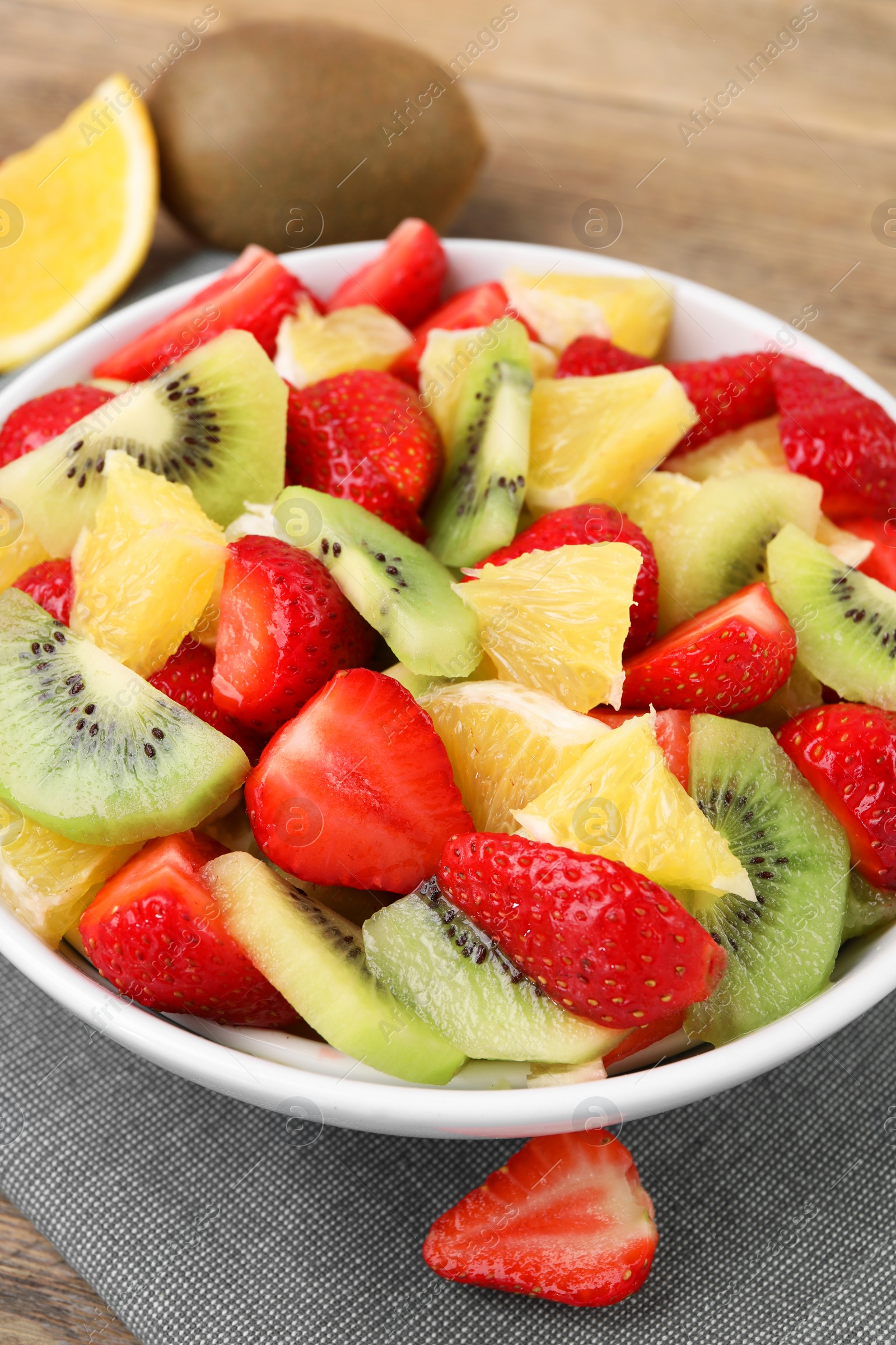 Photo of Delicious fresh fruit salad in bowl on wooden table, closeup