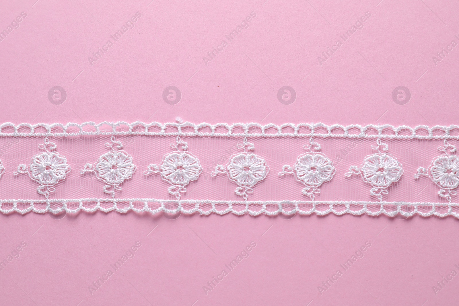 Photo of White lace ribbon on pink background, top view