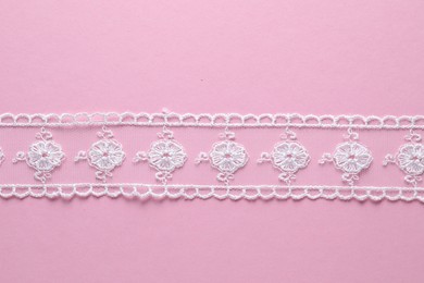 White lace ribbon on pink background, top view