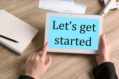 Woman holding tablet with phrase LET'S GET STARTED at table, closeup