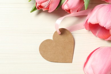 Happy Mother's Day. Beautiful pink tulips with blank heart shaped card on white wooden table, flat lay. Space for text