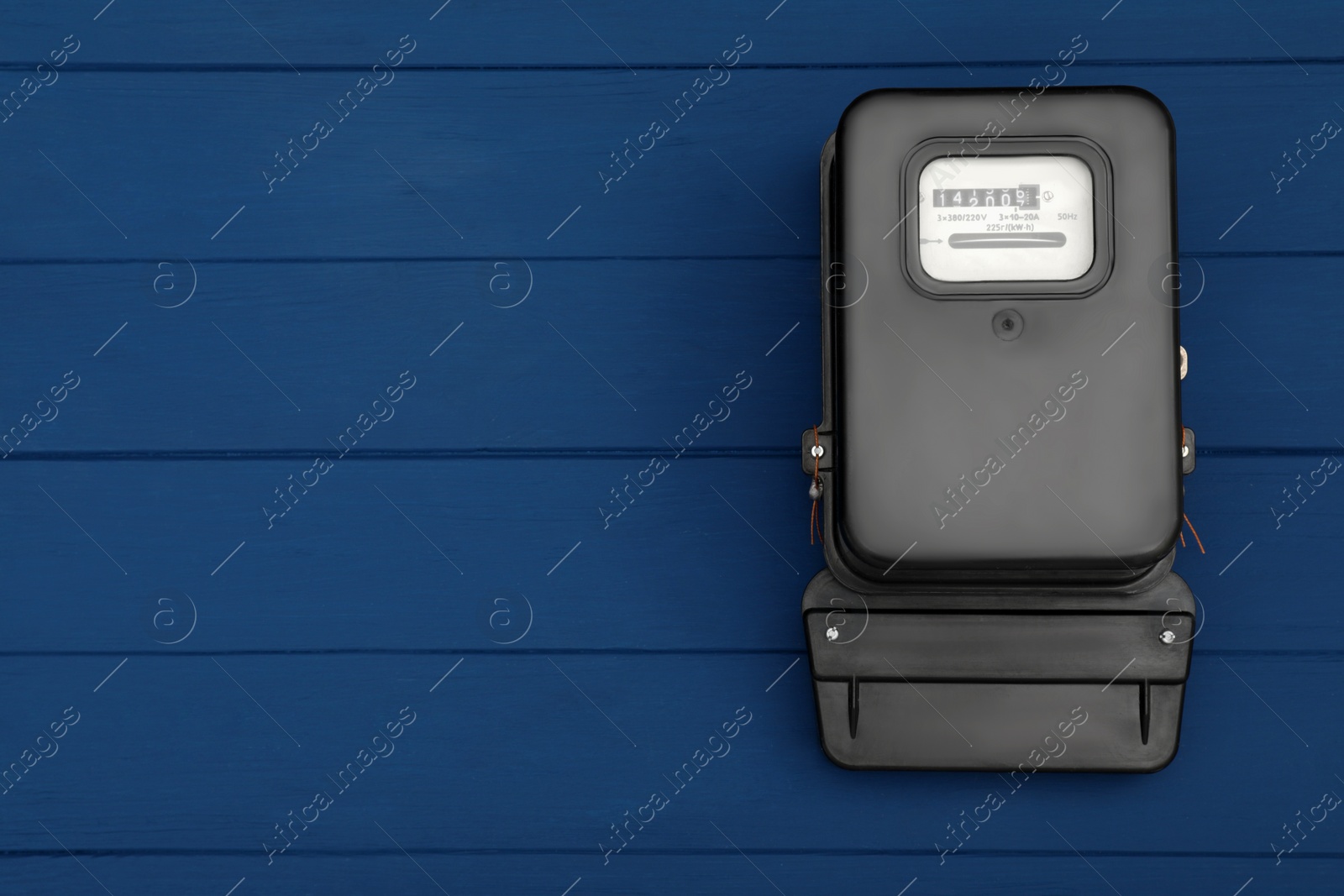 Photo of Black electric meter on blue wooden background, top view with space for text. Measuring device