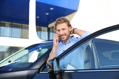 Photo of Young man talking on phone near modern car, outdoors