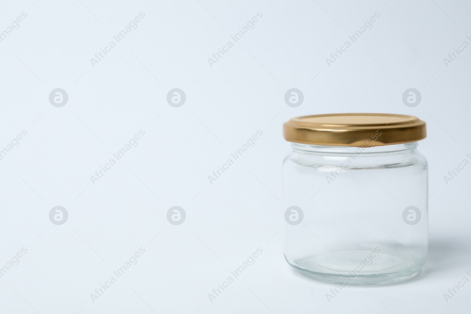 Photo of Closed empty glass jar on light background, space for text