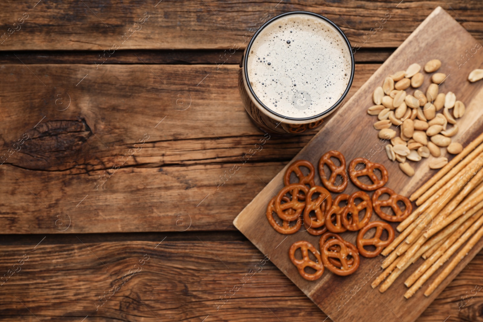 Photo of Glass of beer served with delicious pretzel crackers and other snacks on wooden table, flat lay. Space for text