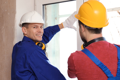 Photo of Workers in uniform installing plastic window indoors