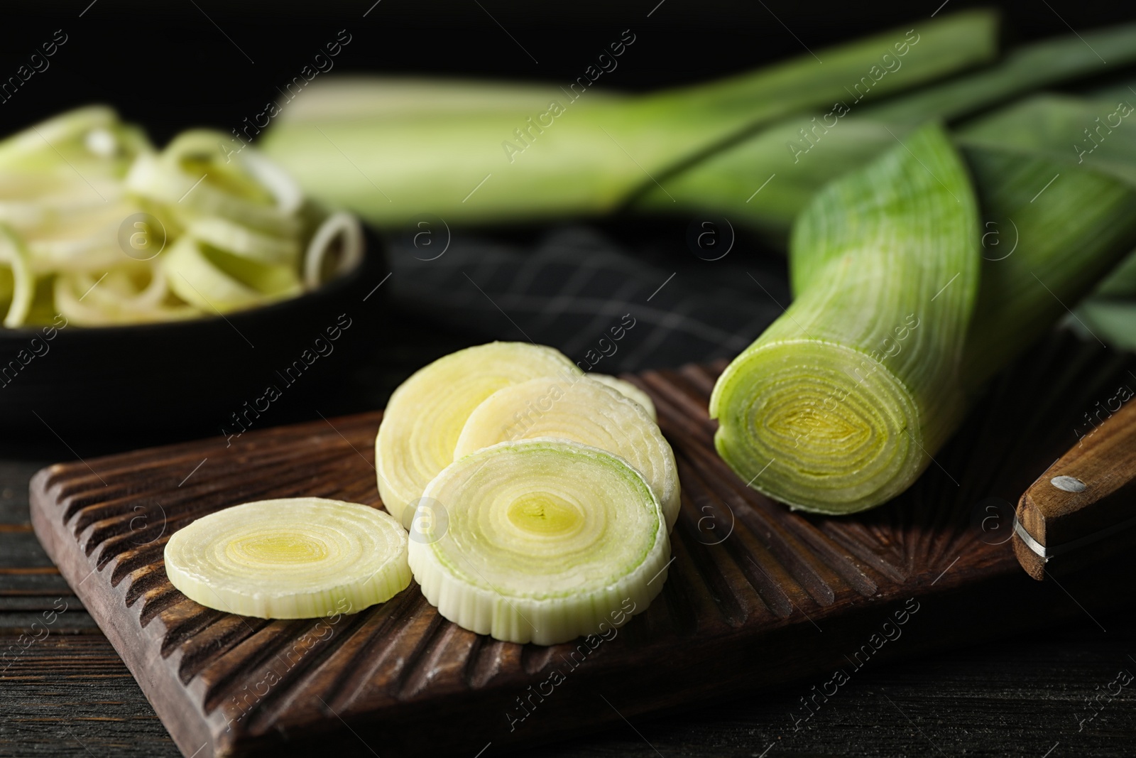 Photo of Fresh raw leeks on black wooden table. Closeup view of ripe onion