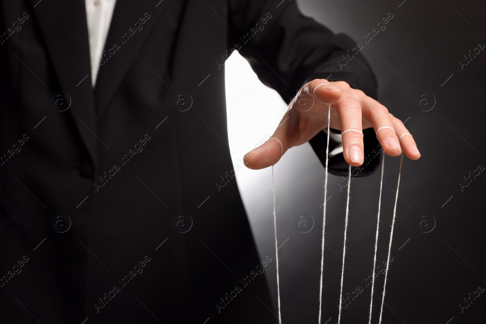 Photo of Woman in suit pulling strings of puppet on dark background, closeup