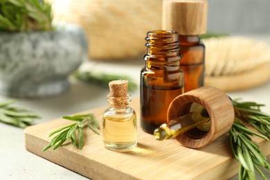 Photo of Essential oils in bottles and rosemary on light gray table, closeup