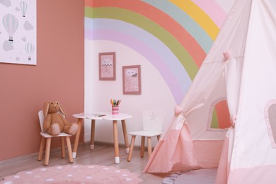 Cute child's room interior with stylish furniture, toy tent and rainbow art on wall