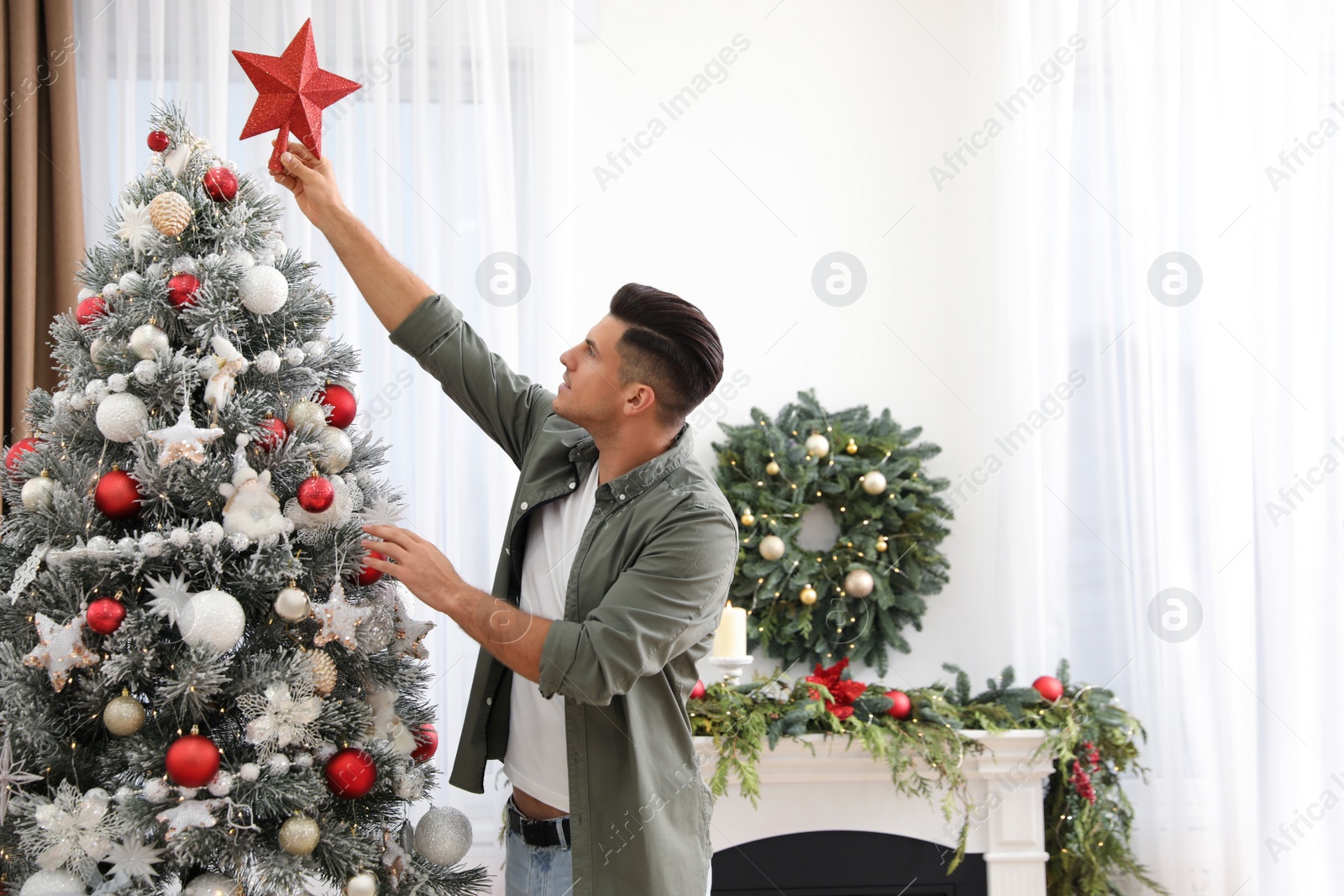 Photo of Man decorating Christmas tree with star topper indoors