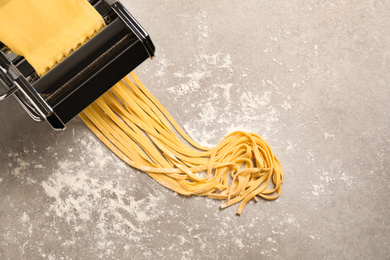 Photo of Pasta maker machine with dough on grey table, top view