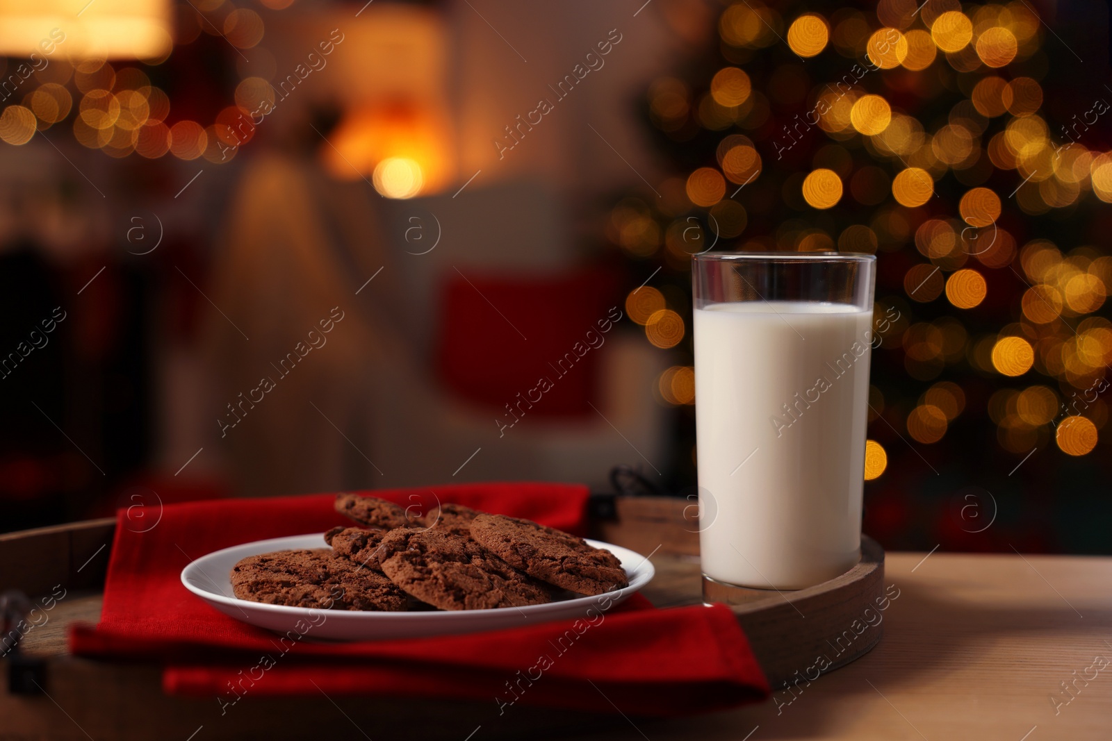 Photo of Milk and cookies for Santa on table in room with Christmas tree. Space for text