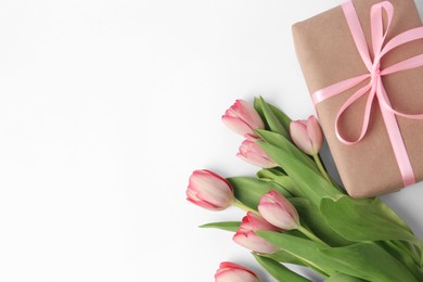 Photo of Beautiful gift box with bow and pink tulips on white background, flat lay. Space for text