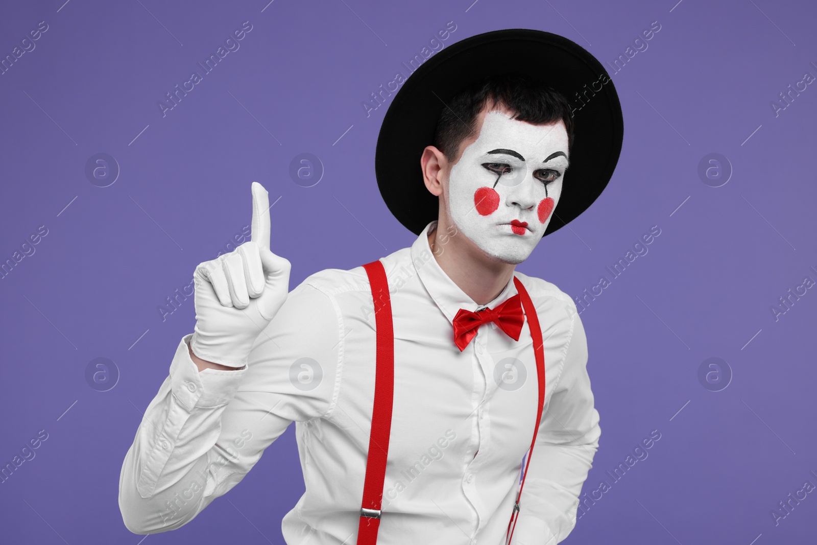 Photo of Funny mime artist gesturing on purple background