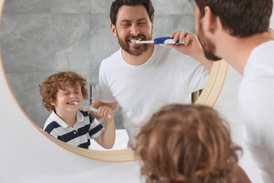 Photo of Father and his son brushing teeth together near mirror indoors