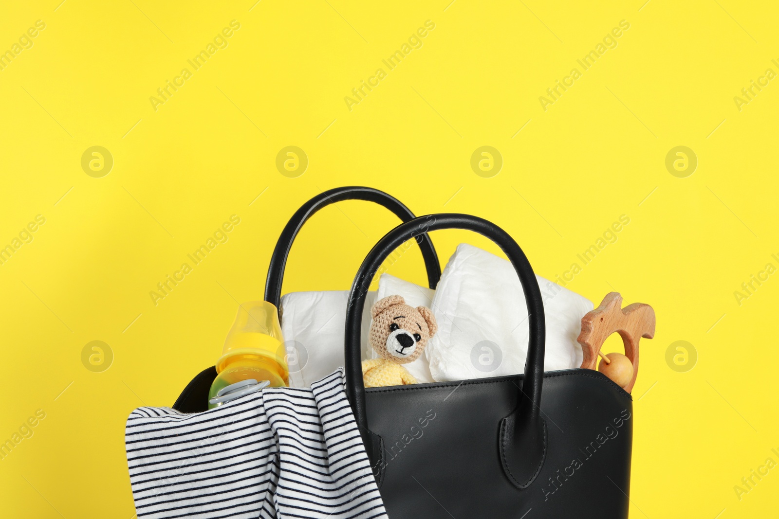 Photo of Mother's bag with baby's stuff on yellow background