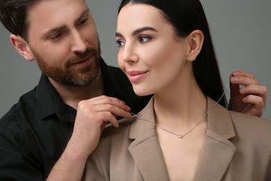 Photo of Man putting elegant necklace on beautiful woman against dark grey background, closeup