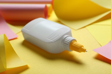 Bottle of glue and colorful paper on yellow background, closeup