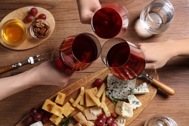 Photo of Women toasting with glasses of wine over cheese plate, top view