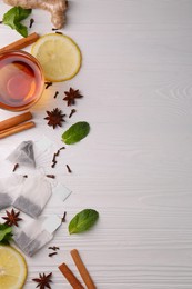 Photo of Tea bags, cup of hot drink and ingredients on white wooden table, flat lay. Space for text