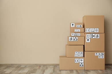 Photo of Cardboard boxes with different packaging symbols on floor near beige wall, space for text. Parcel delivery