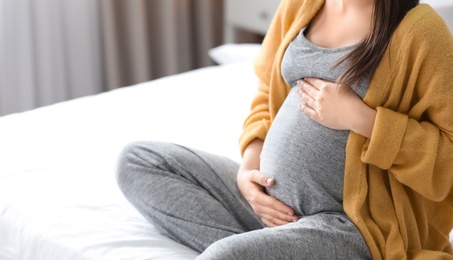 Photo of Young pregnant woman sitting on bed at home