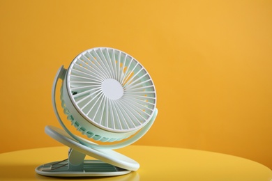 Modern electric fan on yellow table. Space for text