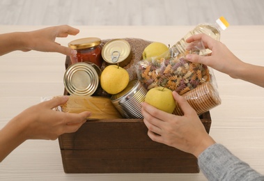 Photo of Women taking food out of donation box on wooden table, closeup