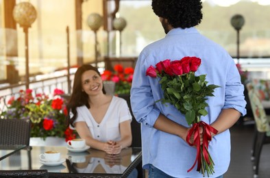 Photo of International dating. Man hiding bouquet of red roses for his beloved woman in restaurant, selective focus