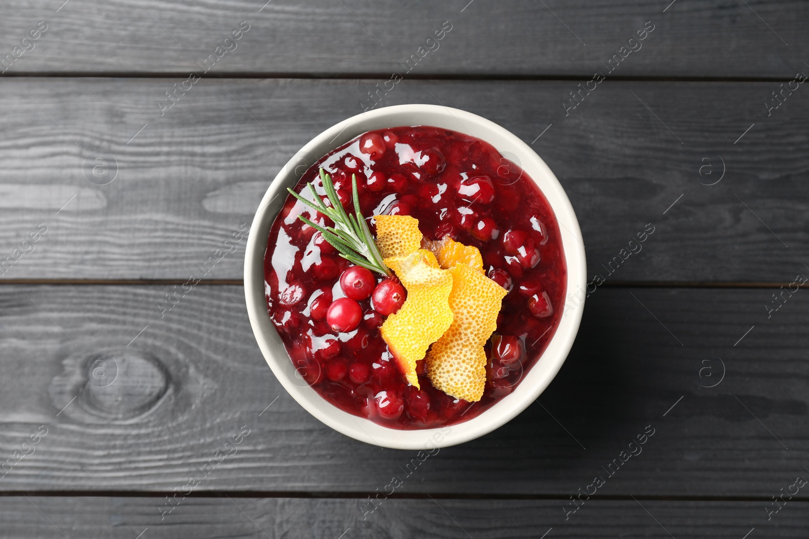 Photo of Fresh cranberry sauce, rosemary and orange peel in bowl on black wooden table, top view