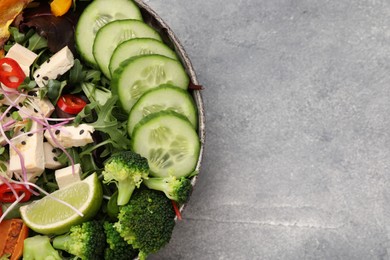Photo of Bowl with many different vegetables and tofu on grey table, top view and space for text. Vegan diet