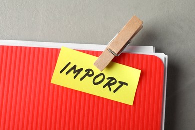 Note with word Import attached to folder of documents on grey table, top view