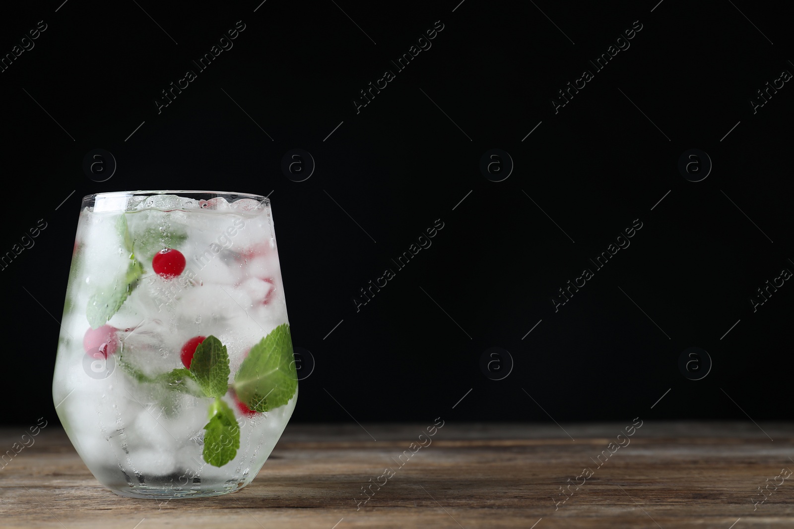 Photo of Vodka cocktail with cranberries and ice on wooden table against black background. Space for text