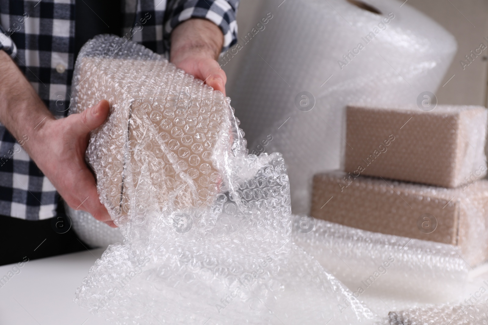 Photo of Man covering box with bubble wrap at table in warehouse, closeup