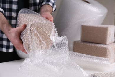 Photo of Man covering box with bubble wrap at table in warehouse, closeup