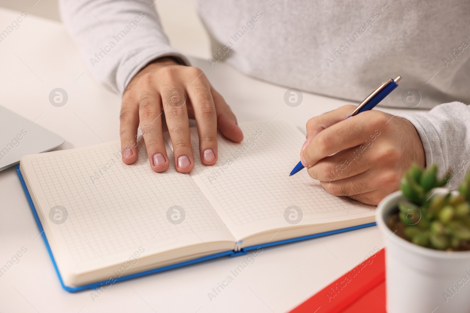 Photo of Young man writing in notebook at white table, closeup