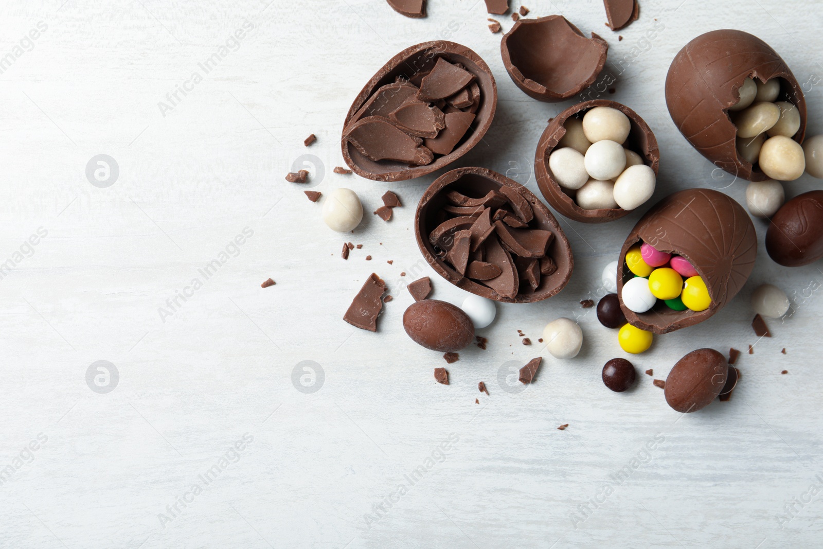 Photo of Broken chocolate eggs with candies on white wooden table, flat lay. Space for text