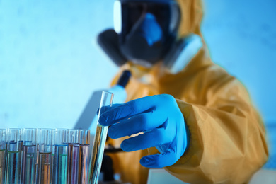 Photo of Scientist in chemical protective suit taking test tube out of rack at laboratory, focus on hand. Virus research