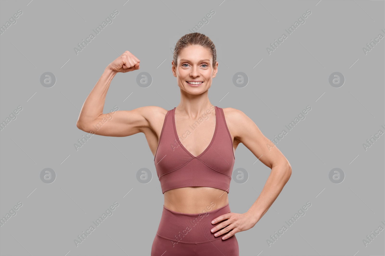 Photo of Portrait of sportswoman showing muscles on grey background